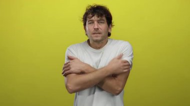 Beyaz tişörtlü İspanyol adam soğuktan titriyor parlak sarı arka planda rahatsız edici ve serin bir ortam sergiliyor..