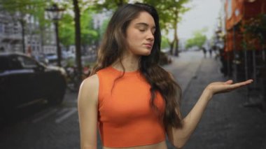 Genç İspanyol kadın yaz güneşinin altında hareketli bir şehir caddesinde sol elini kaldırıyor..