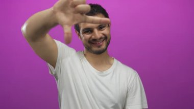 Beyaz tişörtlü adam elleri ile görünümü çerçeveler ve mor stüdyoda gülümseme; yaratıcılık neşe hayal gücü.