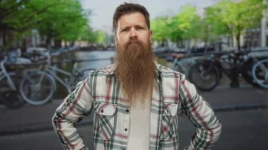 Ekose gömlekli adam, park halindeki bisikletlerle dolu, güneşli kanal caddesinde x jesti yaparak kollarını kavuşturuyor..