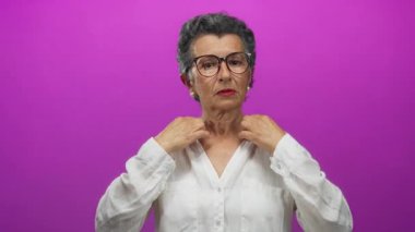 Gri saçlı ve gözlüklü yaşlı bir kadın canlı pembe bir arka plana karşı gevşiyor. Sakin bir ortamda ellerini kişisel bakım ve gerginlik için nazikçe kullanıyor..