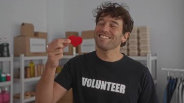 Gönüllü odasında sevinçle gülümseyen kırmızı kalp sembolü taşıyan bir adam..