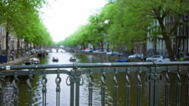 İkonik köprüler ve yeşil ağaçlarla dolu bulanık kanallar bulutlu bir gökyüzünün altında çözünmüş bir şehir manzarasını gösteriyor, canlı şehir yaşamını yansıtıyor..