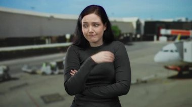 Esmer bir kadın havaalanında sürpriz ve endişeyi dile getiriyor, arka planda seyahat etmeyi simgeleyen görünen bir uçakla yoğun bir seyahat ayarını vurguluyor..