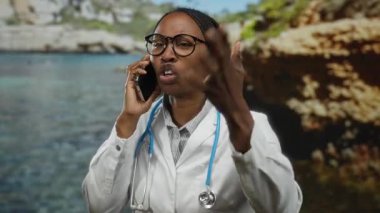 Deniz kenarında hayal kırıklığıyla konuşan, gözlüklü ve doktor önlüklü bir kadın gündüz vakti manzaralı bir plaj ortamında duyguları yakalıyor..