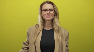 Gözlük takan sarışın kadın, parlak sarı bir arkaplan karşısında düşünceli bir şekilde şakağına el kol hareketi yapıyor. İçgörü ve yaratıcılık hissi veriyor..