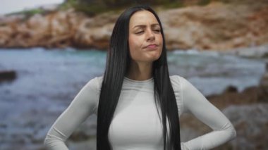 Deniz kenarında düşünceli bir kadın, beyaz elbiseli İspanyol kadın deniz kenarında duruyor, derin düşüncelere dalmış bir ifadeyle, sakin sahil ve suyla çevrili..