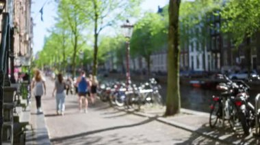Amsterdam 'da güneşli bir kanal caddesinde yürüyen, olay yerini çevreleyen bisikletli, ağaçlı ve binalı insanların sakin bir şehir atmosferini yakaladığı görüntüler..