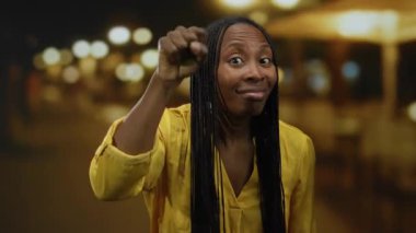 Gece bir şehir caddesinde, uzun saçlı, sarı tişörtlü, bulanık sokak lambalı bir şehir ortamında duygularını ifade eden bir kadın..