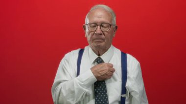 İş kılığındaki kıdemli adam canlı kırmızı arka plana karşı duruyor, ciddi ve kendinden emin, profesyonel ve deneyimli görünüyor..