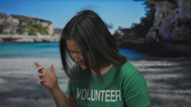 Yeşil gönüllü gömlekli kadın, güneşli bir plajda turkuaz deniz altyapısı olan gitarı neşeli bir şekilde taklit ediyor..