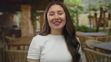 Beyaz tişörtlü kadın, gülümseyerek restoranda el ele işaret veriyor..