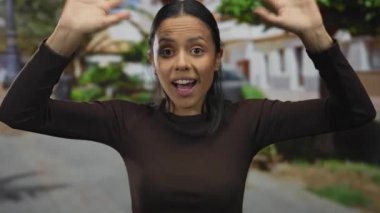 Canlı bir caddede canlı bir şekilde el kol hareketi yapan İspanyol kadın yemyeşil ve mimari detaylarla dolu bir ortamda canlı bir iletişim kuruyor..