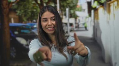 Genç İspanyol kadın her iki işaret parmağını caddede kameraya doğrulturken gülümsüyor; dostça bir davet.