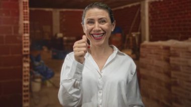 Gülümseyen kadın, binanın içinde beyaz gömlek giyerek baş parmağıyla baş parmak hareketi gösteriyor..