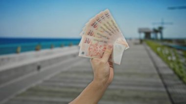 Sahilde, arka planda deniz manzarası olan bir yerde erkek el ele tutuşuyor..