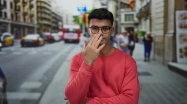 Kentsel caddede gözlüklü genç bir İspanyol gün ortasında kırmızı eşofman üstü giyiyordu. Düşünceli bir ifadeyle şehir hayatının meşguliyetini ima ediyordu..