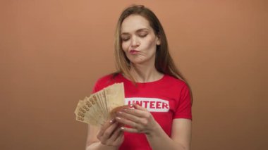 Beyazlı genç bir kadın bej stüdyoda Türk lira banknotları ve yelpaze para sayıyor; şüphecilik.