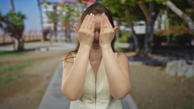 Kadın çerçeveleri elleri ile yüz ve gözleri kapalı gülücükler ağaçlar arasında güneş ışığı parkı yürüyüş yolu; neşe.