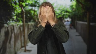 Uzun sarı saçlı, kadife ceketli bir adam sokakta dürbün gibi elleri çerçeveler, merak..