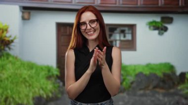 Dışarıda gülümseyen bir kadın kırmızı gözlük takıyor. Siyah, yemyeşil, kentin arka planında gülümsüyor. Arkadaş canlısı, neşeli bir ifade takınıyor.