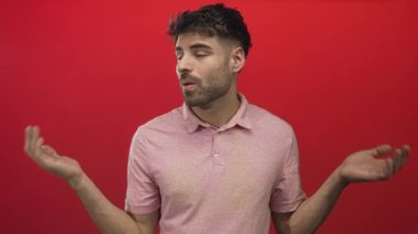 Kırmızı stüdyo ortamında omuz silken adam, şaşkın ifadeyle kaşlarını kaldırdı ve avuçlarını açık bıraktı..