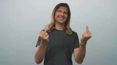 Sarışın ve uzun saçlı bir adam stüdyoda açık mavi duvarın altında orta parmak hareketi gösteriyor..