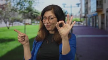 Gözlüklü ve mavi ceketli kadın, tamam işareti elle ve parmağıyla sokakları işaret ediyor..