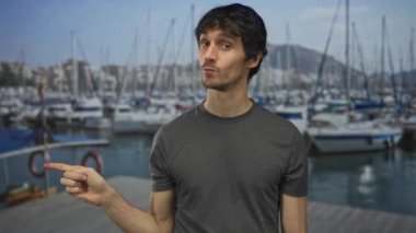 Gri gömlekli adam güneşli bir öğleden sonra güneşli bir gökyüzünün altında modern bir binanın dışındaki tekneleri işaret ediyor..
