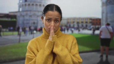 İtalya 'da ikonik sidik kulesinin önünde dua eden kadın güneşli bir günde insanlarla ve binalarla çevrili rahat sarı bir kazak giyiyor..