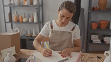 Kadın kağıt üzerine kalem ve el ile çizimler yapar. Stüdyoda çömlek aletleri ve seramik vazolar arasında çalışır. Yaratıcı konsantrasyon..