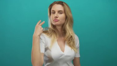 Sarı saçlı genç bir kadın, yeşil arka planda parmakları olan ve enerjik bir şekilde gülümseyen bir sayma hareketi gösteriyor..