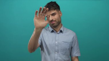 Genç İspanyol adam ciddi bir ifadeyle Teal 'c stüdyosundaki kameraya avucunu dışa doğru itiyor..