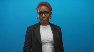 Gözlüklü ve spor ceketli kendine güvenen genç bir kadın parlak mavi bir stüdyoda gözleri işaret ediyor..