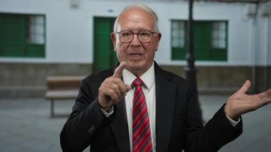 Takım elbiseli yaşlı bir işadamı sessiz bir sokakta parmaklarıyla dışarıda el kol hareketi yaparak kıdemli otorite ve iletişim becerilerini gösteriyor..