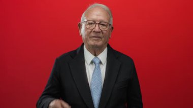 İş dünyasının kıdemli adamı kırmızı bir geçmişe karşı jest yapıyor ve gülümsüyor, profesyonelliği ve pozitif iletişimi somutlaştırıyor..