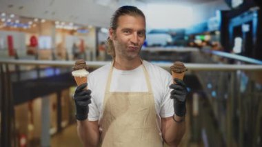 Sarışın adam alışveriş merkezinde iki tane çikolatalı ve vanilyalı dondurma külahını tutuyor ve inceliyor; kararsızlık..