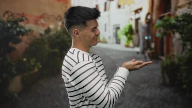 Çizgili süveter giyen genç bir adam çekici bir şehir caddesinde hareketli bir yeşillikle açık hava ortamında kendinden emin ve çekici bir hava yayıyor..