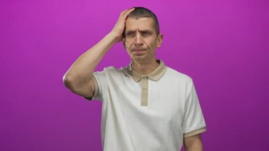 Kafkasyalı bir adam parlak pembe arka plana karşı kafa karışıklığı içinde yalnız başına düşünceli bir ifadeyle dikiliyor ve günlük beyaz gömlek giyiyor..