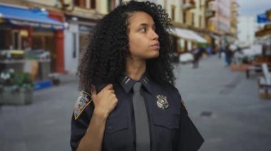 İşlek bir şehir caddesinde kendine güvenen İspanyol polis kadın açık havada ciddi bir ifade ve rozet ile şehir manzarasının ortasında görünür bir üniforma giyiyor.