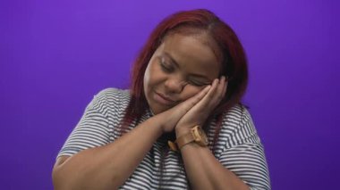 Mor stüdyo duvarına karşı çizgili gömlek giymiş, el ele uyuyan bir kadın..