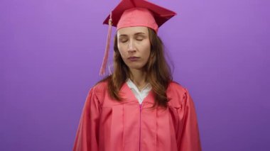 Mezuniyet kepi ve cübbesi giyen bir kadın, izole bir mor arka plan karşısında yukarıya bakıyor, genç mezun olduktan sonra mizahi ve düşünceli bir ifade sergiliyor..