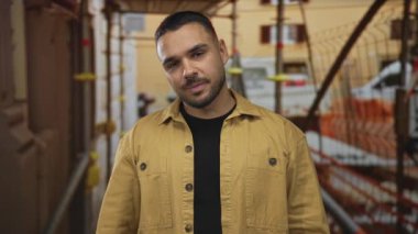 Kahverengi ceketli adam inşaat alanında iskele ve metal kirişler ile açık havada görüldüğü için tırnak işareti yapıyor; şüphecilik.