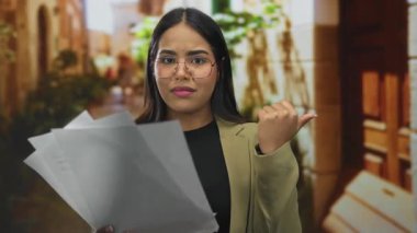 Sokakta elinde kağıtlar tutan bir kadın, şehir zemininde İspanyol kökenini ön plana çıkaran gözlüklü ve spor ceketli bir kadınla kafa karışıklığı yaşıyor..