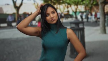Sokaktaki genç İspanyol kadın çevresi insanlarla ve yeşilliklerle çevriliyken fikir jesti yapıyor.