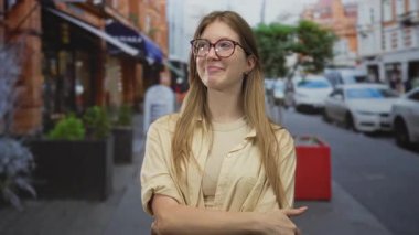 Gözlüklü bir kadın, yoğun bir şehir caddesinde geçen arabaları tararken kollarını kavuşturuyor..