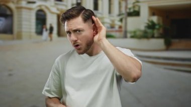 Sakallı genç adam şehir caddesinde dikkatlice dinliyor bulanık bir geçmişi var açık bir günde şehir ortamını tasvir ediyor, merakını ve açık havaya odaklanmasını vurguluyor.