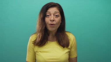 Stüdyo ortamında elleri havada, orta yaşlı İspanyol bir kadın, sarı gömlekli, sürpriz..