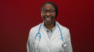 Beyaz önlüklü ve steteskoplu gülümseyen kadın kırmızı duvara dayanmış mutlu profesyonel doktor konseptini gösteriyor.