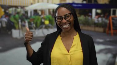 Şehir caddesinde sarı tişört ve gözlüklerle gülümseyen bir kadın, şehir zemininde pozitif titreşimler sergiliyor..